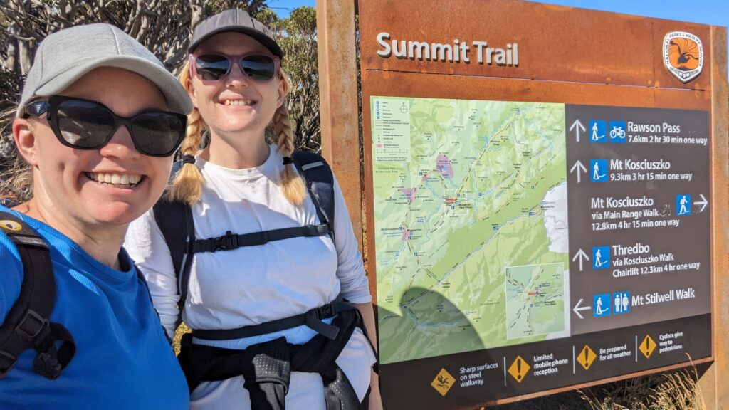 Two blonde white women in hiking clothes, hats, sunglasses, and wearing backpacks, smiling and standing beside the map of the Mt Kosciusko Summit Walk.
Walking with a friend is one of my favourite tools to keep me well and happy. It's the best therapy.